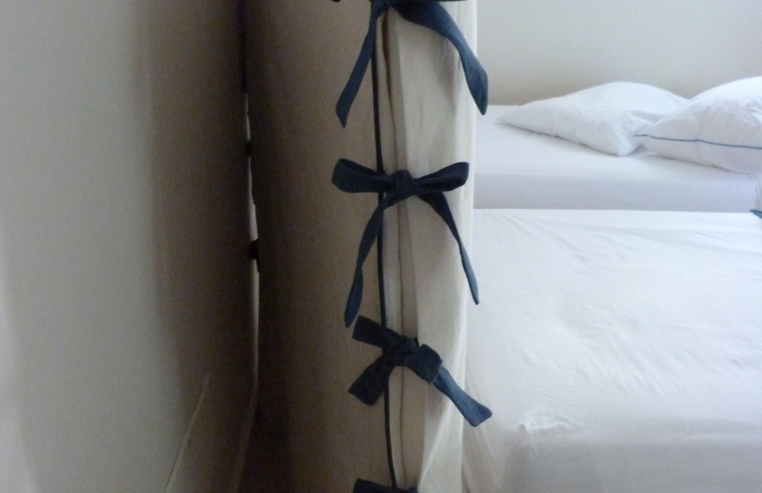 Détail d'une tête de lit en housse avec finition passepoil et nœuds contrastés